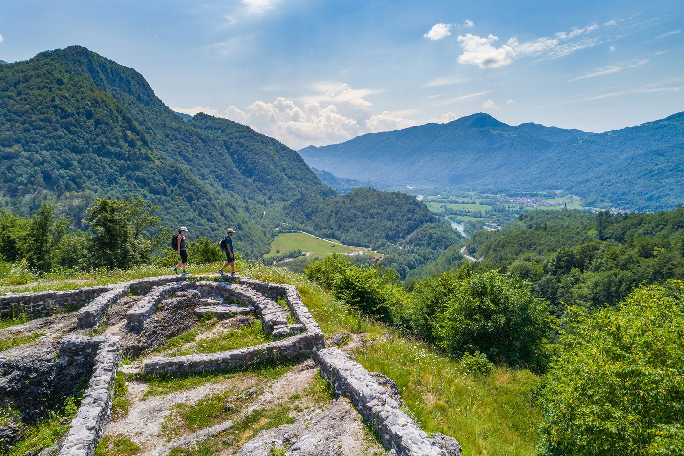 Pohodnika hodita po ostalinah zidu in uživata v ragledu na dolino, kjer teče smaragna reka Soča.