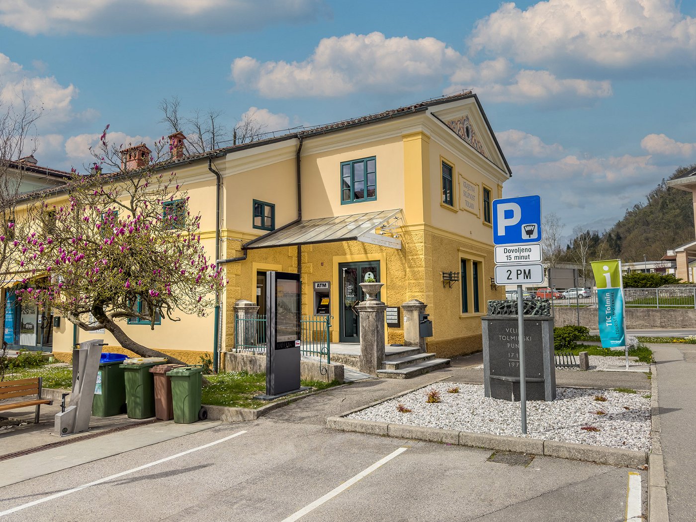 stavba Turističnoinformacijskega centra Tolmin v središču Tolmina, pred katerim je parkirišče za 15 min